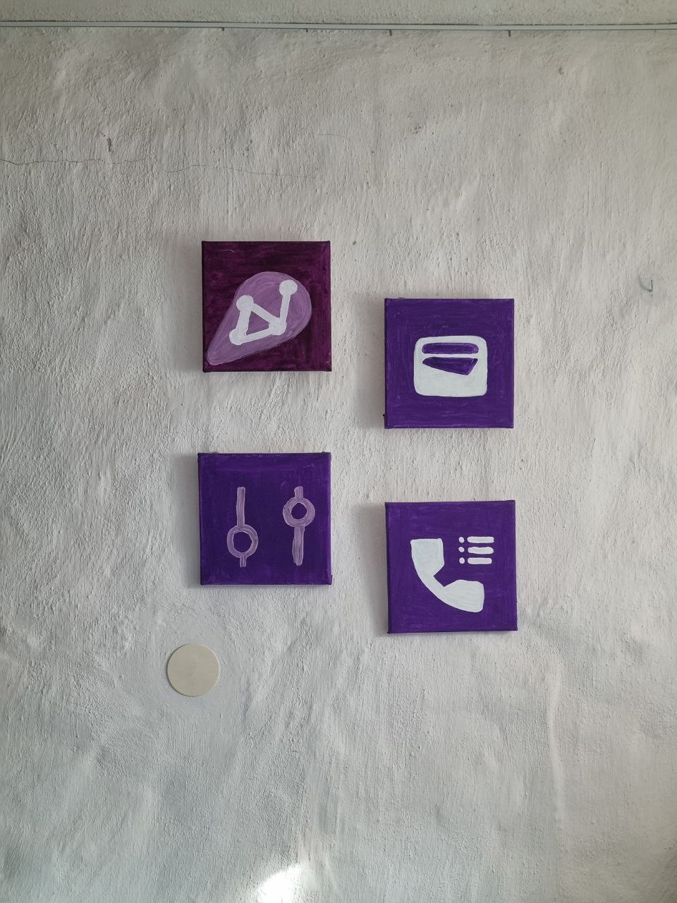 A concrete gallery wall hung with small purple, violet and black acrylic paintings of app icons